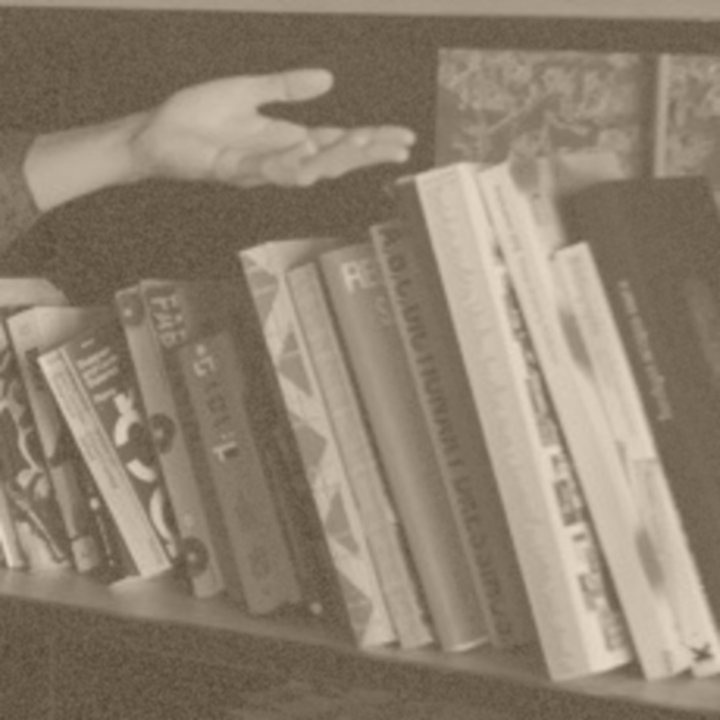 A hand reaching over a shelf of book spines